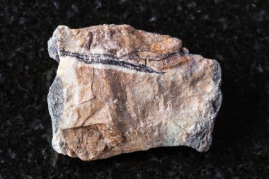 Siyah granit zemin üzerinde işlenmemiş rodonit kaya örneği yakın plan