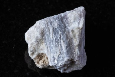 Siyah granit zemin üzerinde kayanın içinde ham rubellit kristali örneği yakın plan.