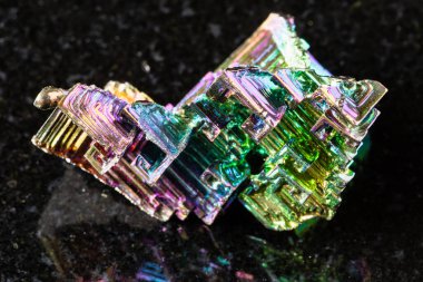 Siyah granit arka planda ham yetişmiş bizmut kristalleri örneği yakın plan