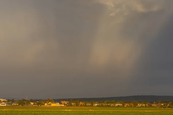 flat landscape with houses and sunrays between dense rainclouds