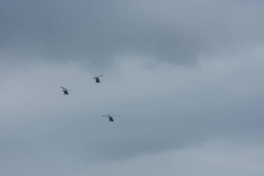 Üç helikopter gri gökyüzünde yağmur bulutlarıyla uçuyor.