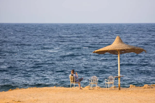 Ενιαία Ομπρέλα Παραλίας Και Ένας Άνδρας Που Κάθεται Στη Θάλασσα — Φωτογραφία Αρχείου