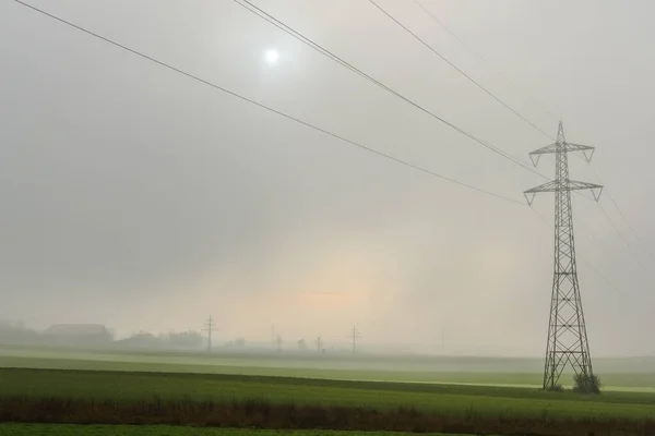 single power pole with dense fog and sun at the sky in the winter
