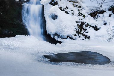 Donmuş su yüzeyinde kışın bir dereden küçük bir şelale.