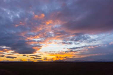 Kışın düz bir arazide gün batımında gökyüzünde mavi ve renkli bulutlar.