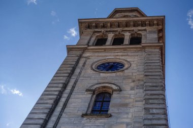 Kiliseden yüksek bir kule, saati ve mavi gökyüzü, beyaz bulutlu, detaylı manzaralı.