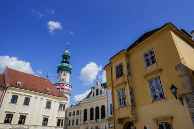 Kilise, mavi gökyüzü ve beyaz bulutlu Hungary 'de bir yerde bir kule ve eski evler inşa eder.