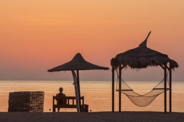 Hamağın yanındaki bankta oturan kadın Kızıl Deniz 'in doğuşunu bekliyor.