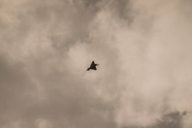 single loud slow flying fighter jet on a cloudy sky clipart