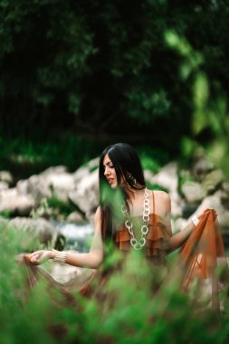 Güzel genç bir kadın yeşil bir çayırda ağaçla poz veriyor.