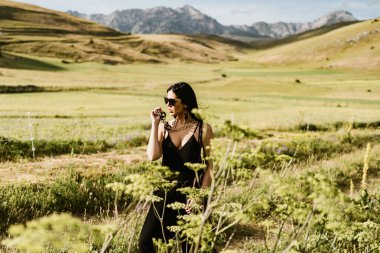 Güzel bir kadının dağda elinde çanta ve kolyeyle yürüyüşünü yakından izle.