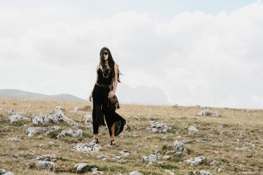 Güzel bir kadının dağda elinde çanta ve kolyeyle yürüyüşünü yakından izle.