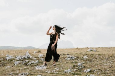 Güzel bir kadının dağda elinde çanta ve kolyeyle yürüyüşünü yakından izle.