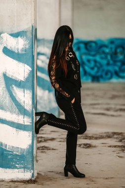 Deri ceketli genç bir kadın ve siyah arka planlı mavi bir elbise.