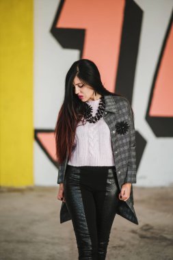 Bir şehir binasının arka planında sırt çantası olan siyah ceketli genç bir kadın.