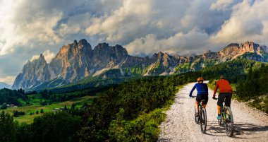 İtalya 'da Dolomitler' de bir kadın ve bir erkek elektrikli dağ bisikletine biniyor. Dağ bisikleti macerası güzel dağ patikalarında.