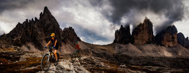 İtalya 'da Dolomitler' de bir kadın ve bir erkek elektrikli dağ bisikletine biniyor. Dağ bisikleti macerası güzel dağ patikalarında.