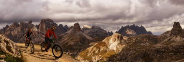 İtalya 'da Dolomitler' de bir kadın ve bir erkek elektrikli dağ bisikletine biniyor. Dağ bisikleti macerası güzel dağ patikalarında.