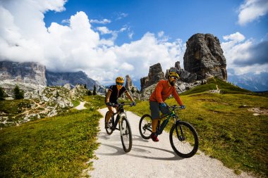 İtalya 'da Dolomitler' de bir kadın ve bir erkek elektrikli dağ bisikletine biniyor. Dağ bisikleti macerası güzel dağ patikalarında.