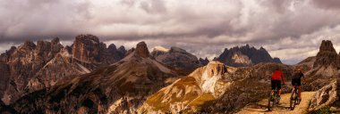 İtalya 'da Dolomitler' de bir kadın ve bir erkek elektrikli dağ bisikletine biniyor. Dağ bisikleti macerası güzel dağ patikalarında.