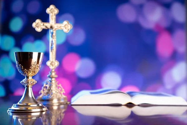 Catholic religion concept. Catholic symbols composition. The Cross, monstrance,  Holy Bible, rosary and golden chalice on blue bokeh background.