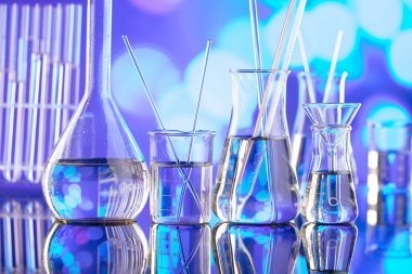 Covid 'e karşı test ve ilaç ile ilgili laboratuvar araştırmaları. Mavi bokeh arka planda cam tüpler ve beherler.