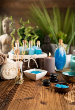 Spa and wellness concept. Bottles with bath and spa cosmetics, rolled up towels, bath salts and care products on wooden rustic paneling.