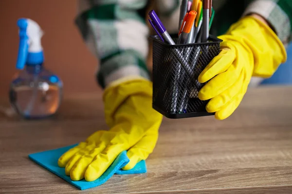 Woman cleans office in the yellow gloves wipes the dust off the office desk.