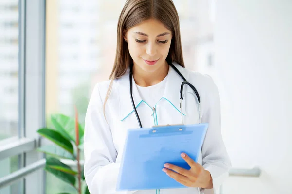 Female Doctor In Surgery Reading Patient Notes.