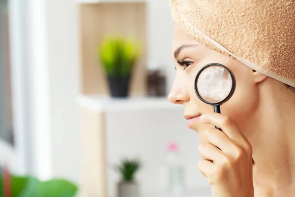 Beautiful face of a young woman with clean fresh skin holding a magnifying glass.
