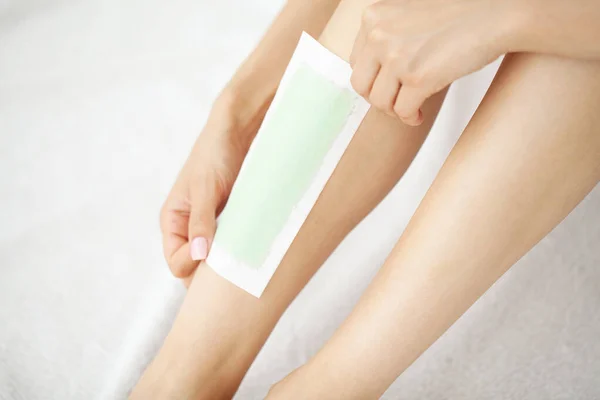 Young woman depilating her leg with wax stripe at home.