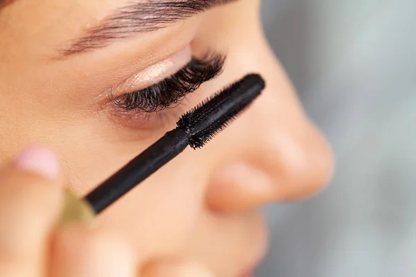 Woman doing morning makeup routine putting mascara in bathroom mirror at home.