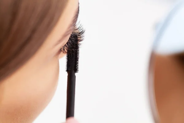 Woman doing morning makeup routine putting mascara in bathroom mirror at home.