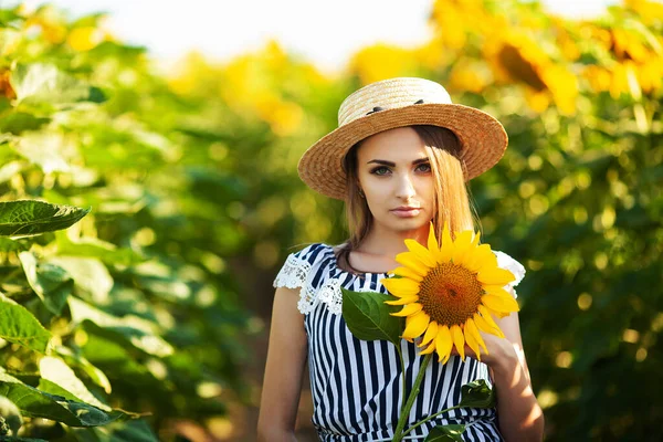 美しいですブロンド女性で花のフィールドで日没で麦藁帽子 — ストック写真