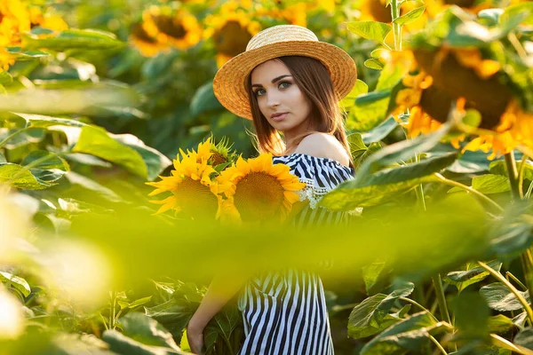 夕暮れ時のひまわり畑で夏を楽しむ帽子の若い女性 — ストック写真