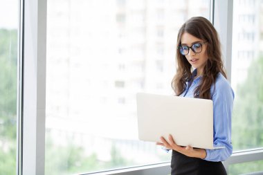 Genç ve güzel bir iş kadını, modern ofiste dizüstü bilgisayarla çalışıyor..