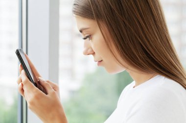 Kafasından vurulmuş genç bir kadın cep telefonu ekranına bakıyor..