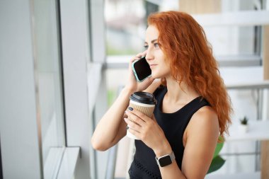 Cep telefonuyla konuşan kızıl saçlı kadın uzaktan bilgisayarla çalışıyor..