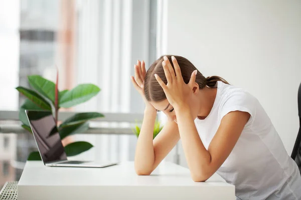 Beautiful stressed young office worker sitting at desk holding head because of pain in office.