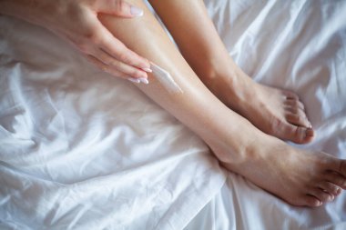 Bacaklarına vücut losyonu süren genç bir kadın..