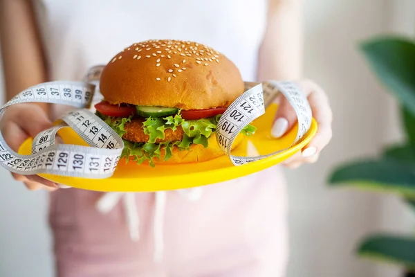 Женщина Держит Вредный Жирный Бургер Измерительной Лентой — стоковое фото
