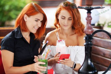 İki genç tatlı kız terasta bir yaz günü bir kafede nargile içiyor..