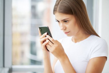 Akıllı telefon ekranına bakan çekici bir kadın, medya haberleri okuyor..