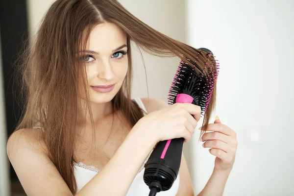 Woman drying hair with hair dryer and round brush