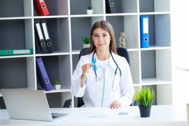 Doktor, yaşayan ve hastalığa yakalananları desteklemek için açık mavi kurdele tutuyor.