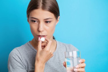 Kadın elinde hap ve cam su tutuyor, baş ağrısı, mide ağrısı veya vitamin alıyor..