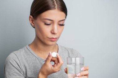 Kadın elinde hap ve cam su tutuyor, baş ağrısı, mide ağrısı veya vitamin alıyor..