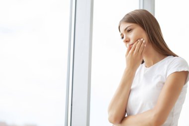 Kadın diş ağrısı çekiyor ve masasında otururken yanağına dokunuyor..