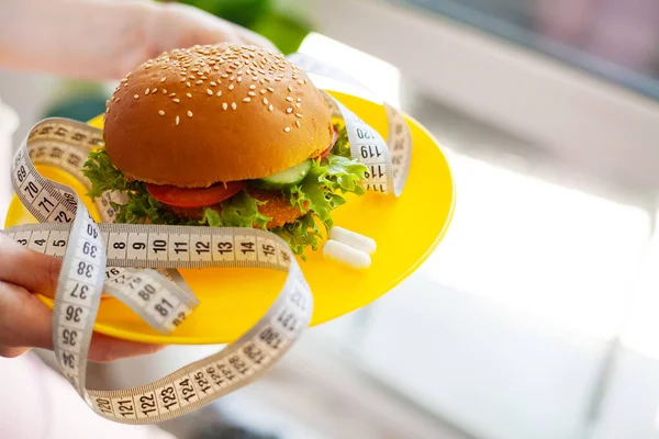 用白色测量带捧着有害脂肪汉堡的年轻女性形象 — 图库照片