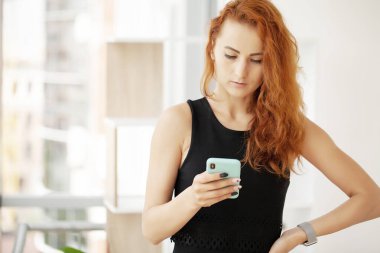 Kızıl saçlı bir kadın ofiste telefonla konuşuyor..